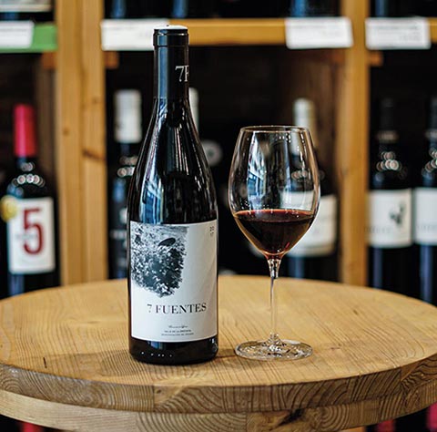 Botella de vino tinto acompañada de una copa, sobre una mesa de madera de DVI vinoteca.